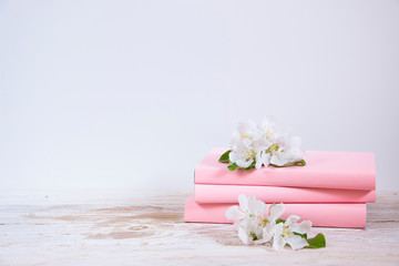 Pink books with white flowers of an apple tree on a light wooden table. Home interior with spring decor.