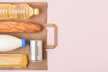 Bottles of oil and milk, spaghetti, tin can, baguette on the light pink background. Safe food delivery. Craft package and essential food set. Copy space on the right. Flat lay.