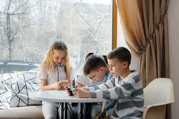 Children sit at a table in a cafe and play mobile phones together. Modern entertainment