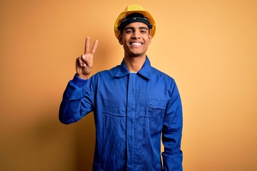 Young handsome african american worker man wearing blue uniform and security helmet showing and pointing up with fingers number two while smiling confident and happy.