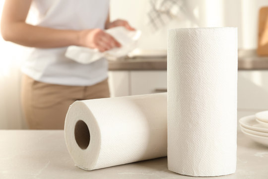 Woman wiping plate with towel in kitchen, focus on paper rolls