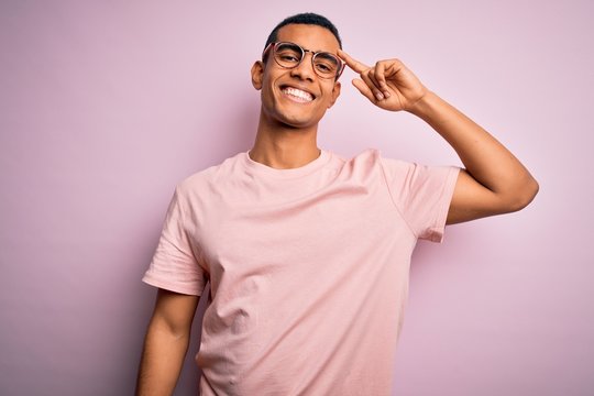 Handsome african american man wearing casual t-shirt and glasses over pink background Smiling pointing to head with one finger, great idea or thought, good memory