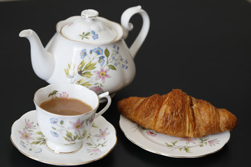 Continental breakfast with a teapot on a black table