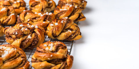 Several homemade baked Swedish cinnamon rolls or kanelbulle on a cooling rack. White background with copy space to add text.