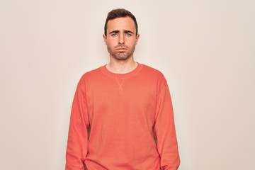 Young handsome man with blue eyes wearing casual sweater standing over white background depressed and worry for distress, crying angry and afraid. Sad expression.