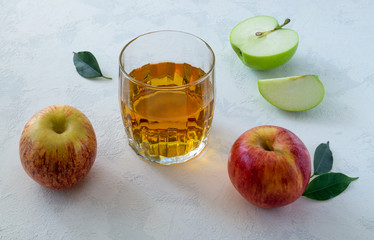 Apple juice in a faceted glass and a few ripe apples on a light blue surface. Concept healthy eating, healthy lifestyle. Selective focus, horizontal orientation.