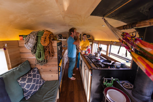 two people drinking beverage inside converted school bus with ropes