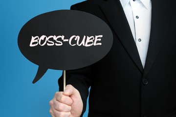 BOSS-CUBE. Mann im Anzug hält Sprechblase in der Hand. Der Text BOSS-CUBE steht im Schild. Blauer Hintergrund. Geschäftsmann für Business, Finanzen, Statistik