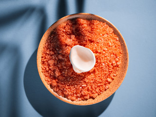 Orange bath salt in a saucer with shells on a blue background with a shadow from a tropical plant....