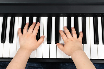 Hands of a young child playing the piano. Learning to play the piano. Studying at home. To stay home. View from above.
