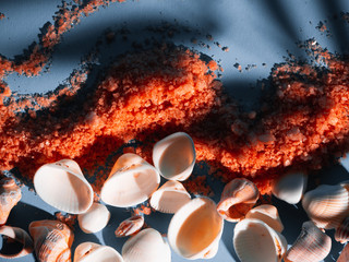 Orange bath salt in a saucer with shells on a blue background with a shadow from a tropical plant. Copyspace, flatlay. Spa, relaxed, summer