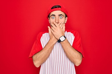 Young handsome sporty man with blue eyes wearing striped baseball t-shirt and cap shocked covering mouth with hands for mistake. Secret concept.