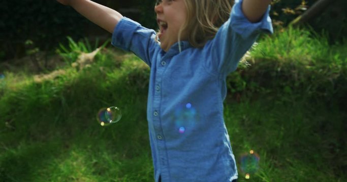Little preschooler boy chasing bubbles on the lawn in spring
