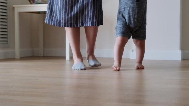 Baby boy takes first steps and learns how to walk barefoot at home with his mother. Slow motion