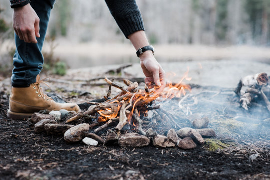 man putting logs on a handmade campfire outdoors in Sweden