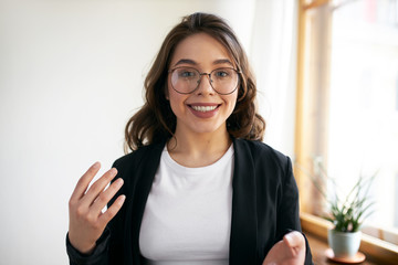 Beautiful positive young woman blogger recording course or workshop for her followers. Cute girl in eyewear chatting from home making video call using webcam and wirelesshigh speed internet connection - obrazy, fototapety, plakaty