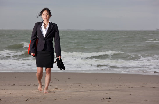 business woman walking on empty beach holding her shoes