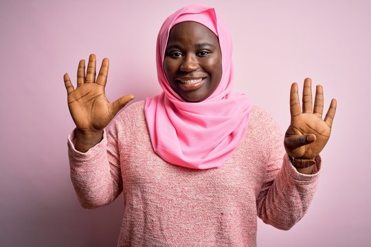 Young african american plus size woman wearing muslim hijab over isolated pink background showing and pointing up with fingers number nine while smiling confident and happy.