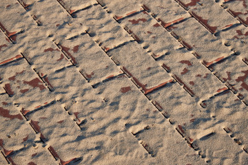 Paving slabs covered with sand in the rays of the setting sun. Background