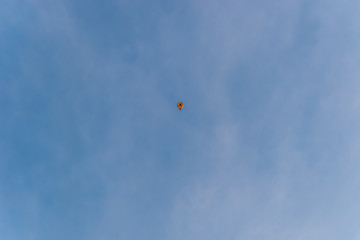 A minimalist shot of a small yellow hot air balloon floating high in the clear blue sky in winter