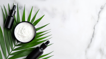 Flat lay jar of organic cream, palm leaf and dropper bottles on marble background. Top view SPA...