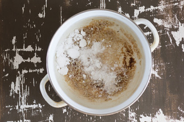 Top view of pan with burnt bottom after cooking porridge and soda in it on the brown background