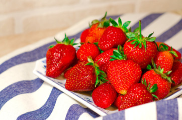 Ripe red strawberries in a white plate on a blue-and-white striped kitchen napkin. The first spring harvest of berries.