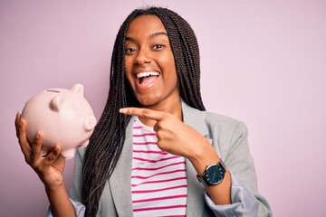 Young african american business woman saving money on piggy bank over isolated background very...