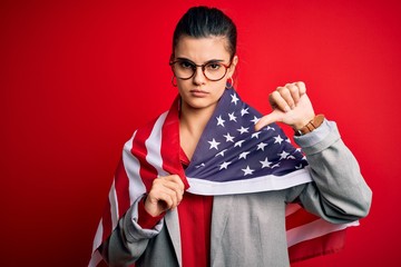 Young beautiful brunette patriotic woman wearing usa flag celebrating independence day with angry...