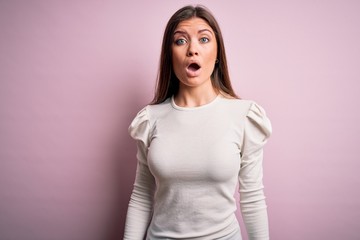 Young beautiful woman with blue eyes wearing casual white t-shirt over pink background afraid and shocked with surprise and amazed expression, fear and excited face.