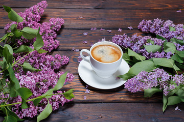 Obraz na płótnie Canvas White cup of coffee a bouquet of lilac lies on a dark wooden background. Fallen lilac flowers on the table. Space for Text. selective focus. Valentine's Day and Mother's Day background.