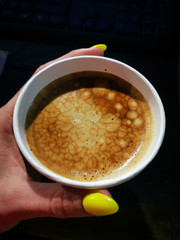 Female hand holds coffee coffee with cream in a paper cup
