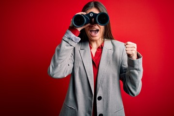Young beautiful woman with blue eyes using binoculars over isolated red background screaming proud and celebrating victory and success very excited, cheering emotion