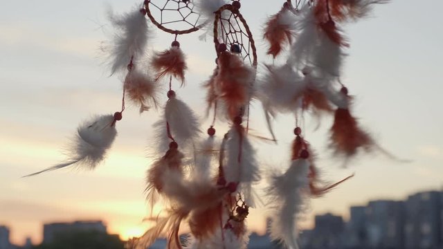 Dreamcatcher with orange feathers, swaying with light wind slow motion slide agains blue sky at sunset in summer. Amulet boho style, Indian style. Bright disk of the sun, the rays of the sun