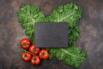 Kale salad leaf and red tomatoes with water drops on an old rustic metal tray. Green nature background. Black stone chalk board for copy space