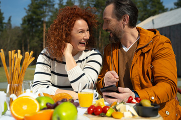 Happy married couple using cellphone during breakfast outdoors