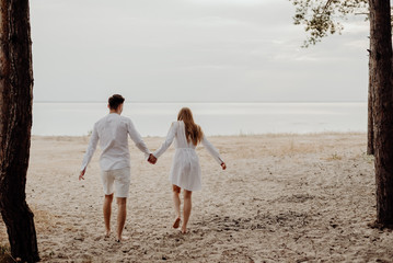 Lovers boy and girl bare feet walk on the sandy shore towards the sea at sunset