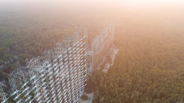 Drone flight over duga 3 radar antenna in the Chernobyl exclusion zone. Secret missile military area with sunset sun and surrounded by forest	
