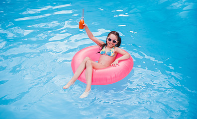 Delighted child with fruit beverage chilling in pool
