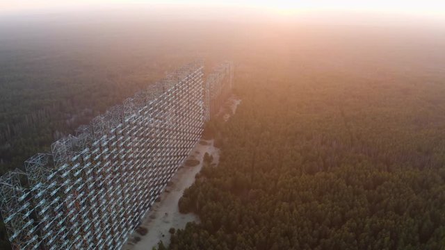 Drone flight over duga 3 radar antenna in the Chernobyl exclusion zone. Secret missile military area with sunset sun and surrounded by forest	