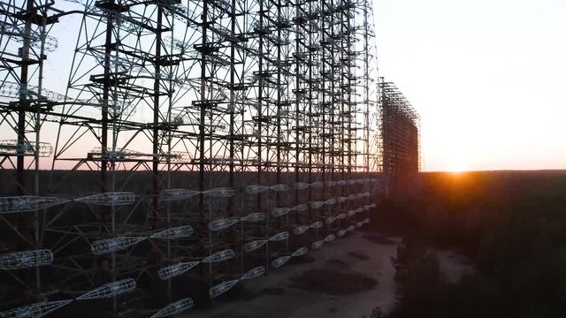 Drone flight over duga 3 radar antenna in the Chernobyl exclusion zone. Secret missile military area with sunset sun and surrounded by forest	