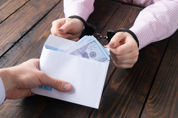 men's hands give money in envelope to women's hands in handcuffs against the background of a wooden table