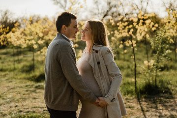 happy young pregnant couple walks in the park,husband holds the hand of his pregnant wife,future dad and mom,walks in the park after quarantine