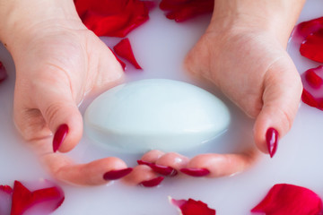 Close up emale hands hold soap against the background of milk or white water with rose petals