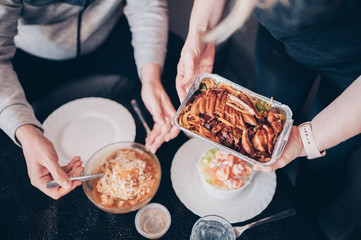 Top view of a woman holding a metal container with Chinese food and her partner ready to eat in unfocused background. Eating at home during isolation by Covid19.Family together