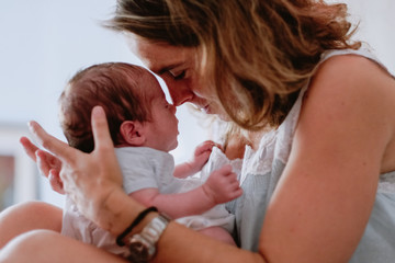 From above closeup of loving mother holding adorable newborn baby while sitting on bed at home