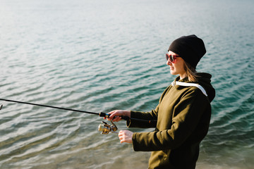 Fisherman with rod, spinning reel on river bank. Sunset. Fishing for pike, perch, carp. Woman catching fish, pulling rod while fishing at weekend. Girl fishing from beach lake or pond with text space.