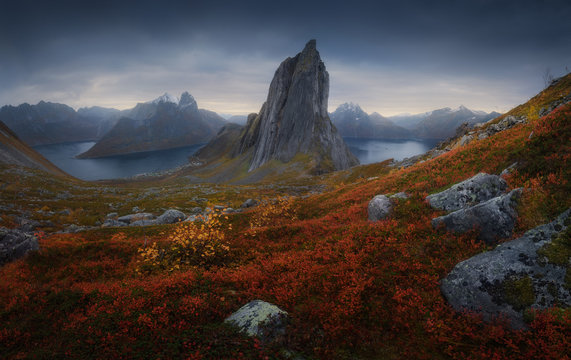 Segla mountain located in grassy valley near calm basin against dark overcast sky on island of Senja, Norway