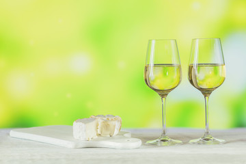 Two glasses of white wine served with cheese board on light green background. Wine mood concept