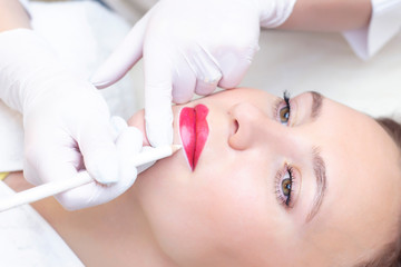 Young woman having permanent makeup on her lips at the beauticians salon. Permanent Makeup (Tattoo). drawing a contour with a white lip pencil